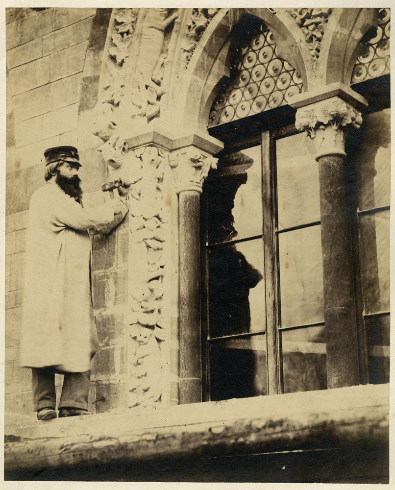 Black and white photograph of a stone mason carving one of the Museum's windows