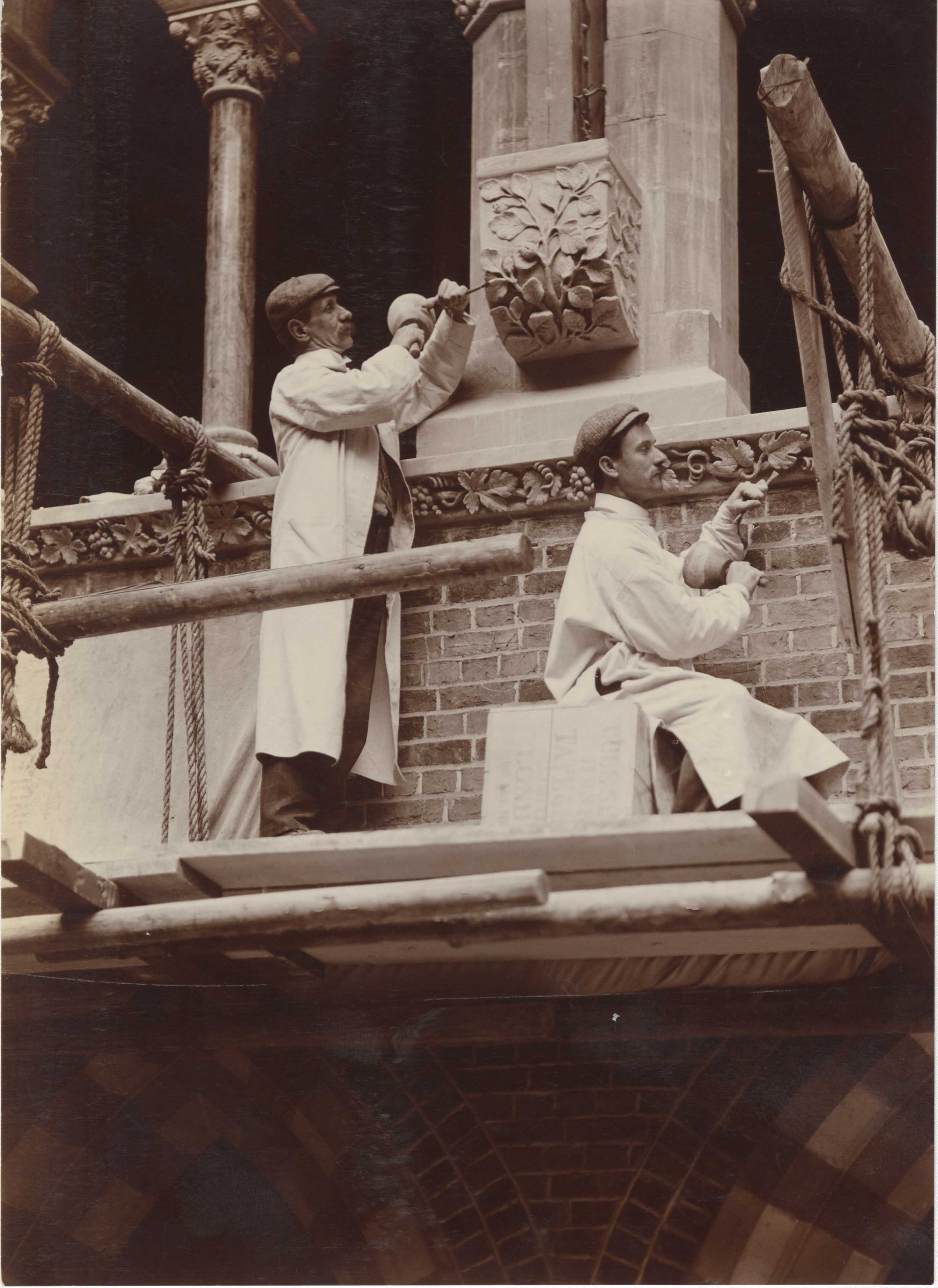 Black and white photo of two stone masons carving botanical decoration 